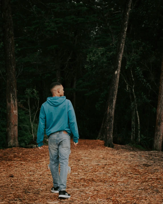 a young man standing in a clearing near some trees