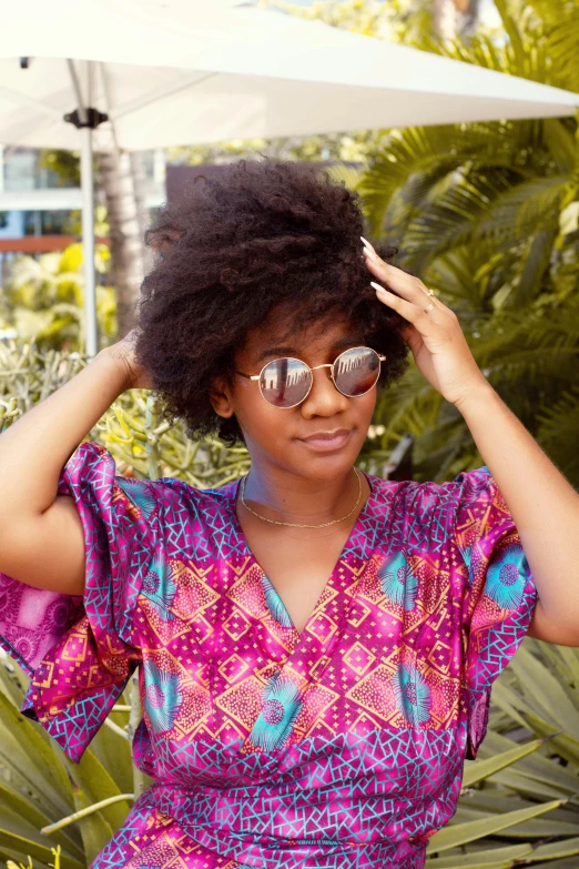 a woman in a colorful dress with sunglasses standing under an umbrella