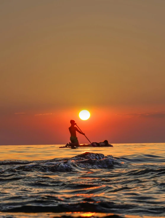 man paddleboarding on large body of water at sunset