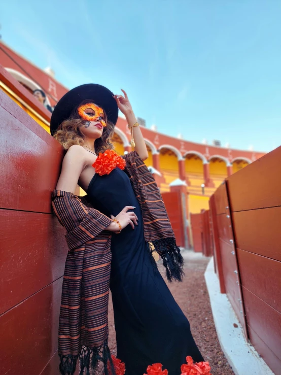 a woman wearing a costume, a hat and scarf leaning against a red wall