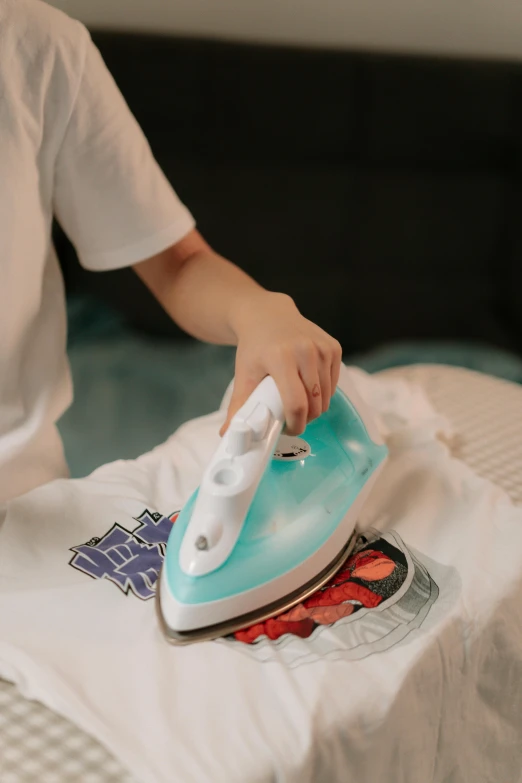 the person is ironing a t - shirt with a hand held iron