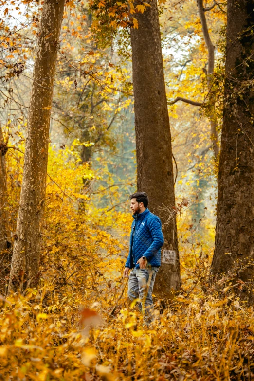 a man standing in a wooded area, holding a rope