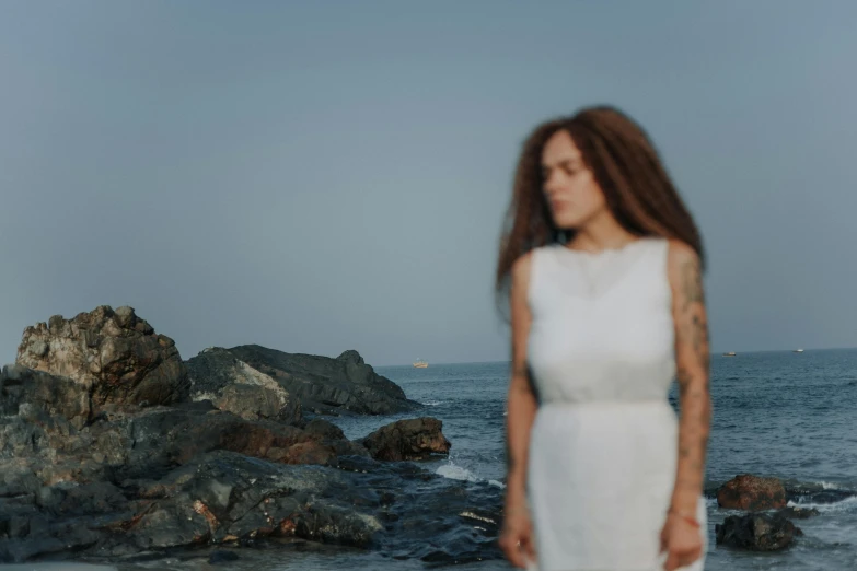 woman in white dress standing at edge of beach, overlooking sea