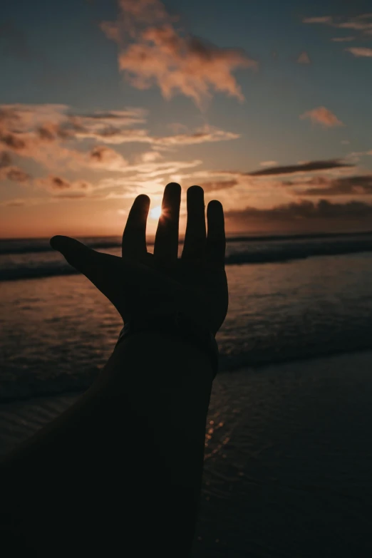 a hand reaching towards the sun in front of a body of water