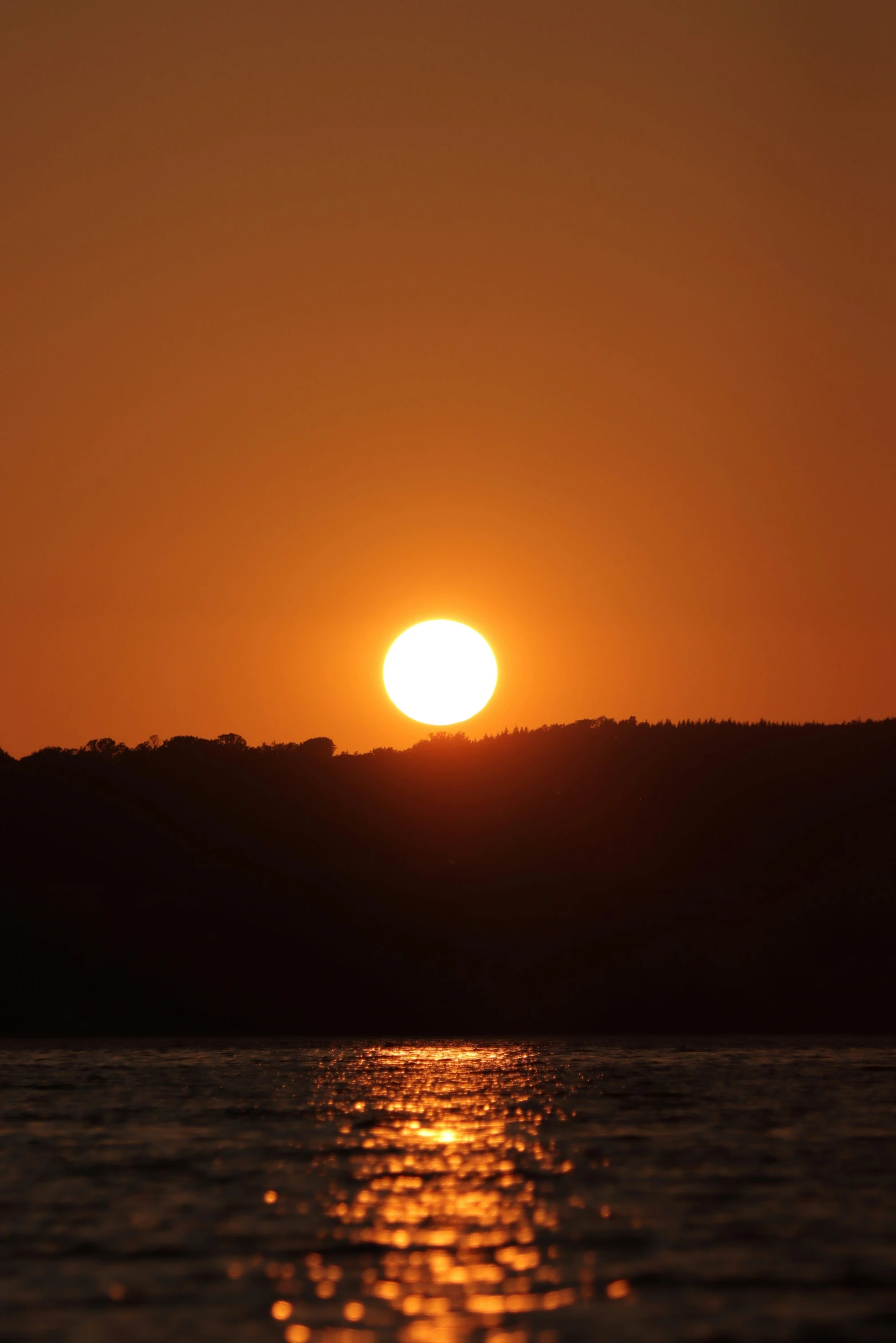 the sun is rising behind a hill on the ocean