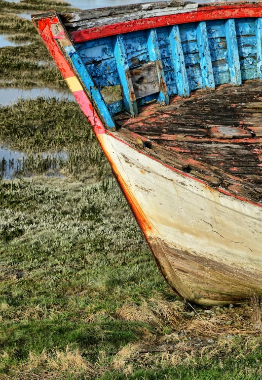 a dilapidated, multicolored boat sitting in the grass