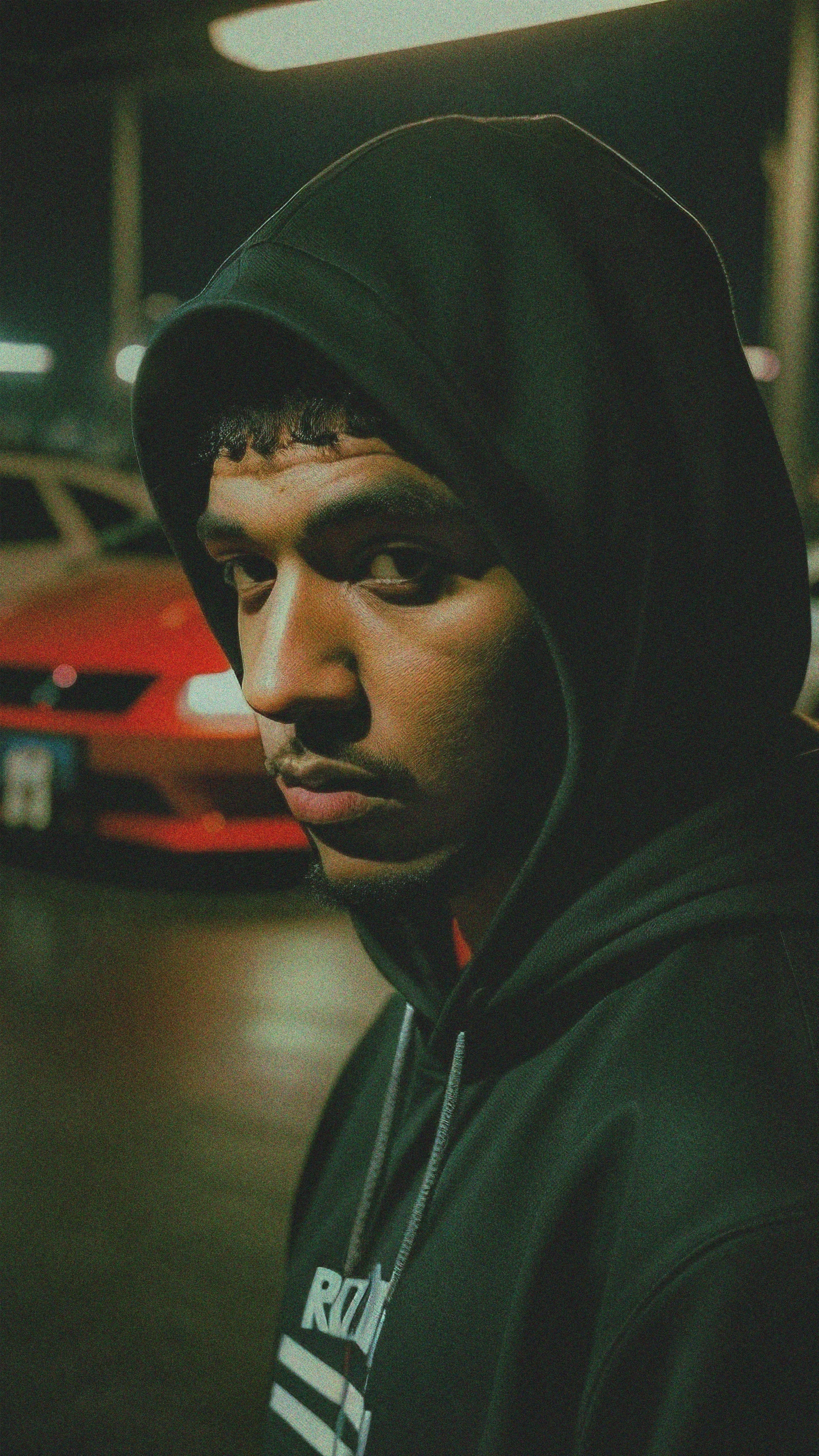 a man with a hood up in front of red cars