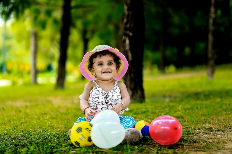 little girl with colorful balloons and hat on grass