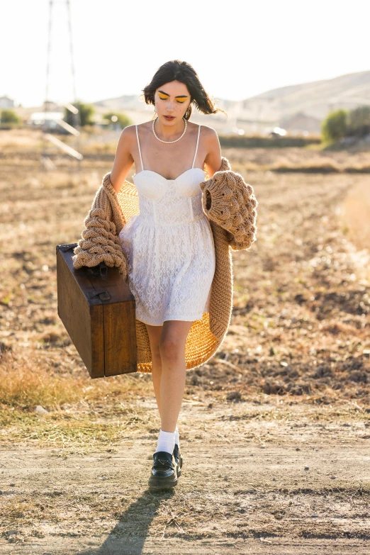 woman in white dress walking in desert with brown suitcase