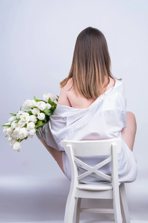 the back view of a woman sitting in a chair holding flowers