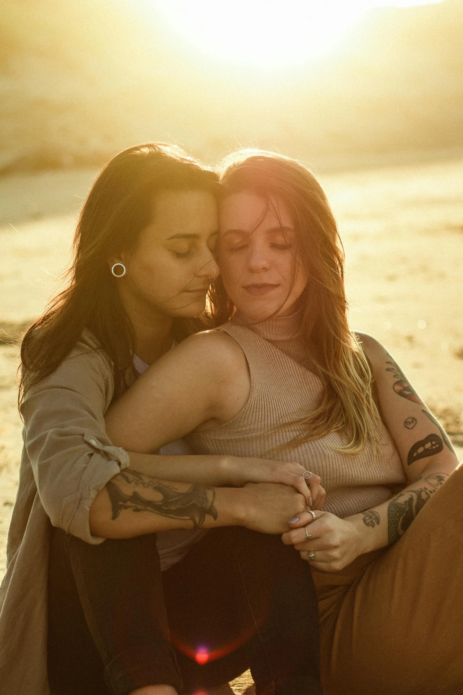 two women sitting on the beach at sunset with the sun setting behind them