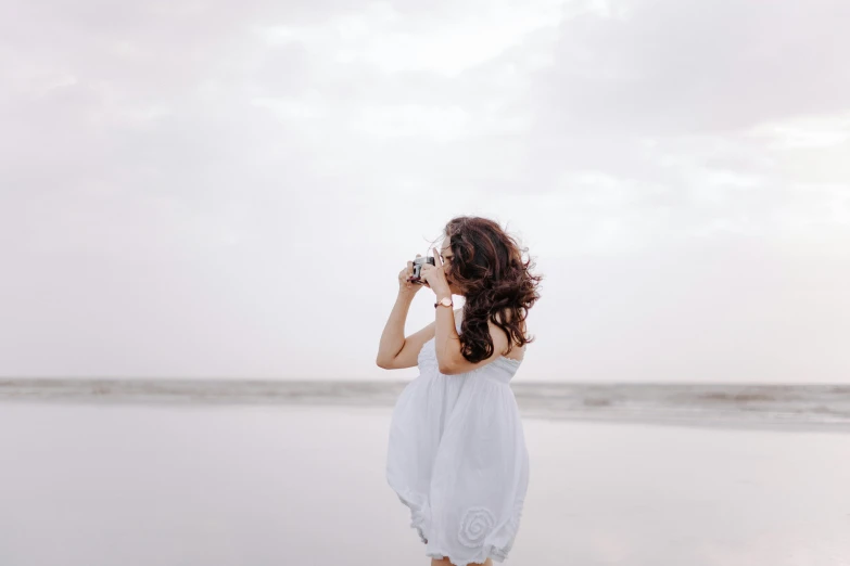 a woman in a white dress on the beach taking pictures