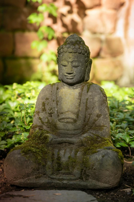 statue in the grass next to brick wall and green vegetation