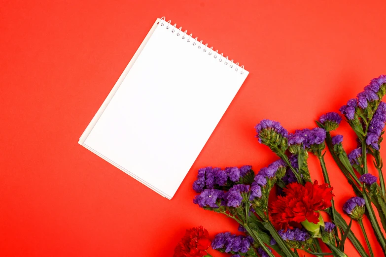 a notepad and purple and red carnations sit beside a bunch of flowers
