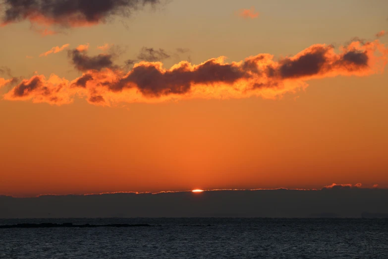 the sun setting on the ocean with the cloud above