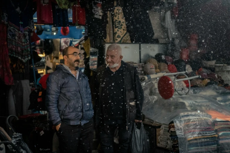 two men are standing outside and talking under a rain shower