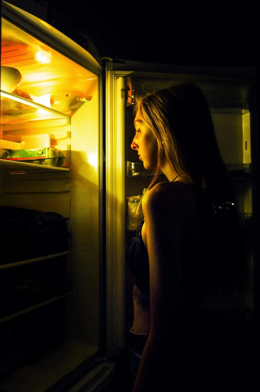 woman in dark lighting lightening up a refrigerator with no one inside