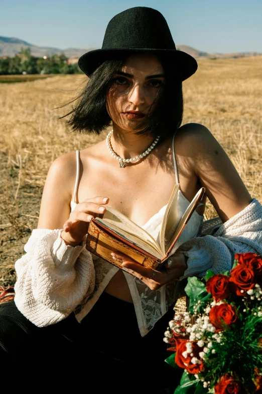 a person with long hair and wearing a hat holds a book in his hands