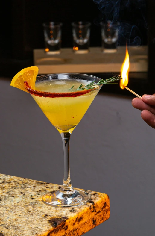 a person holding up a cigarette next to a cocktail in a martini glass