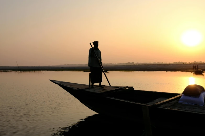 a silhouette of a man with a gun stands in front of a boat in the water