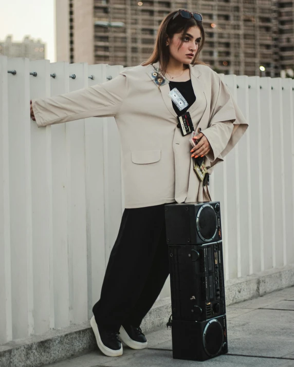 a woman standing by a white fence holding a suitcase and hat