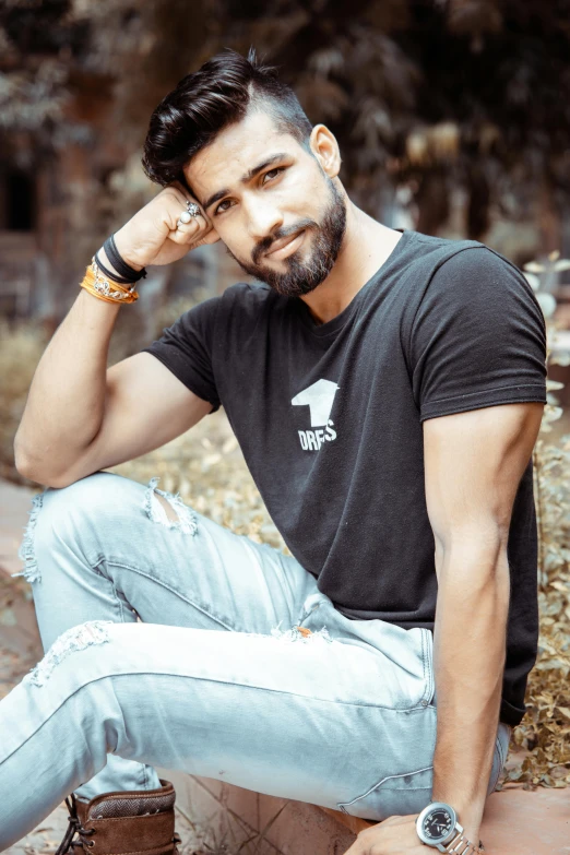 a man sits on a brick ledge wearing blue jeans and a black t - shirt