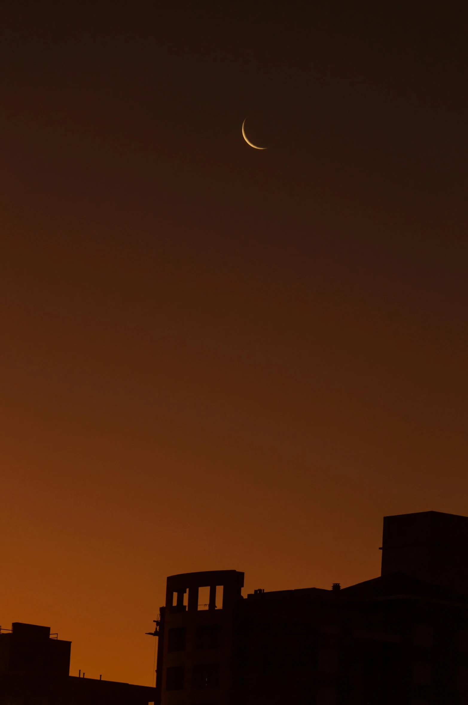 the sun sets behind some buildings and a distant crescent