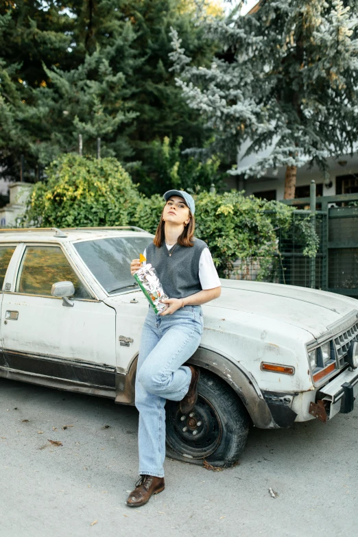 the girl has a flower in her hand leaning on the bumper of a rusty car