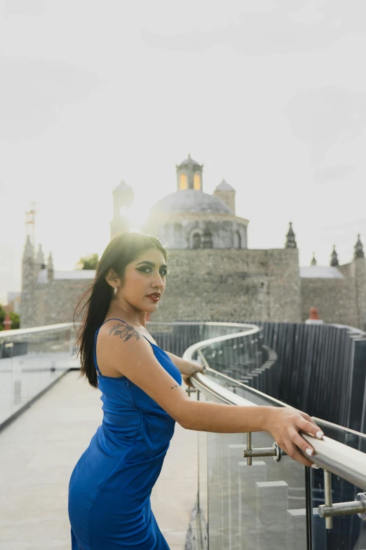 a woman in a blue dress leaning on railing