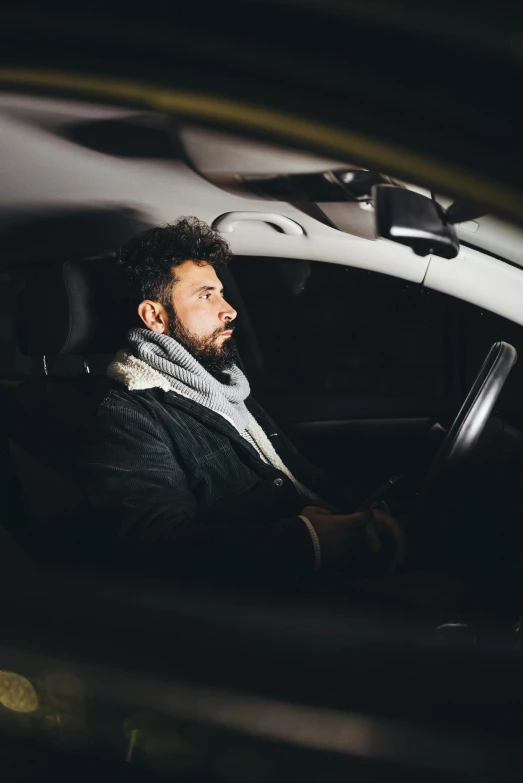 man in black coat sitting inside car with cell phone
