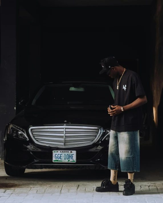 a man in jeans standing next to his black mercedes