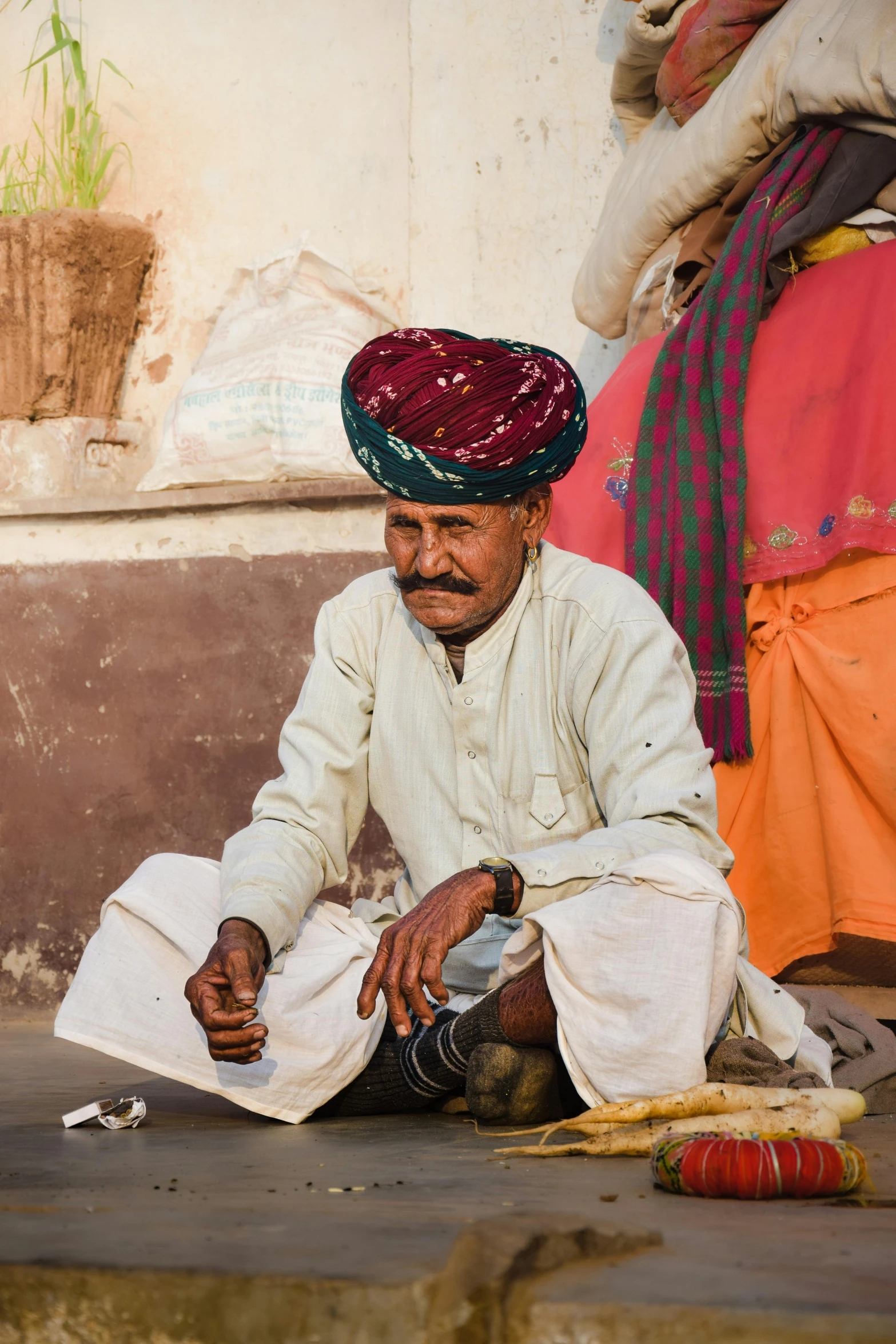 the man sits in front of the wall wearing a hat and scarf