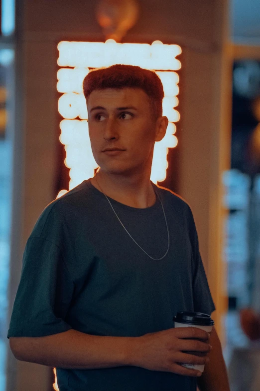 young man standing with a drink under a lighted sign
