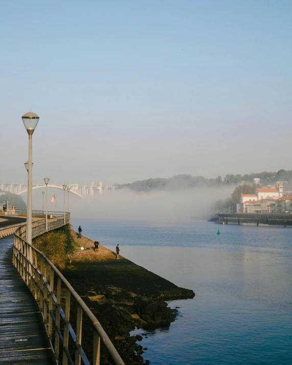 fog is over the water near a boardwalk by some lights