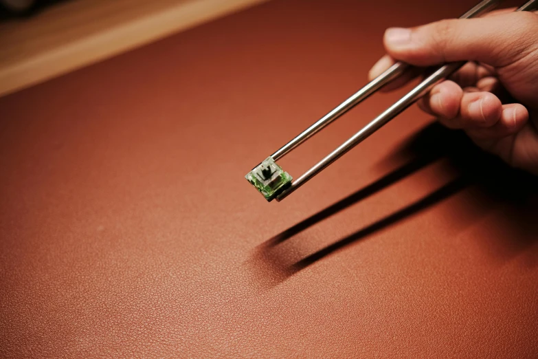 some tongs holding a green piece of electronic