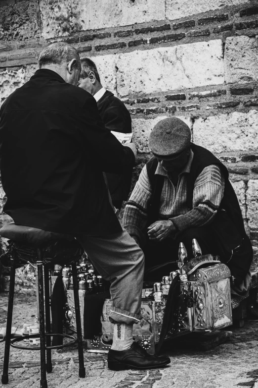 two men sitting down eating while another man sits on a stool