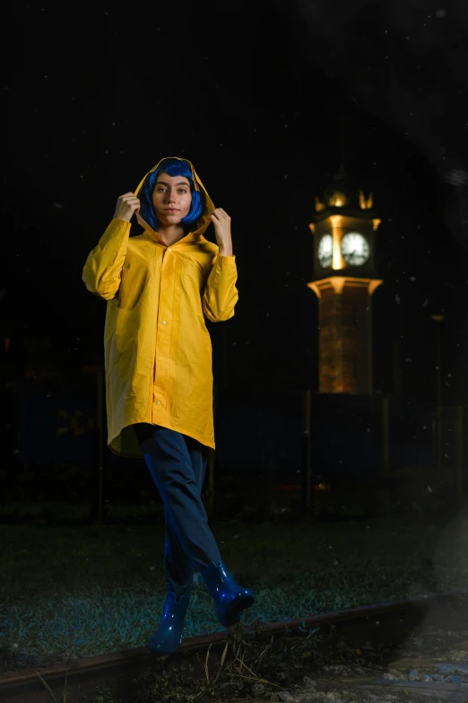 a woman in yellow jacket with blue pants and hat standing on street