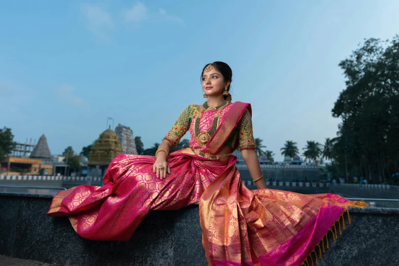 a woman wearing a long pink saree, standing by the road