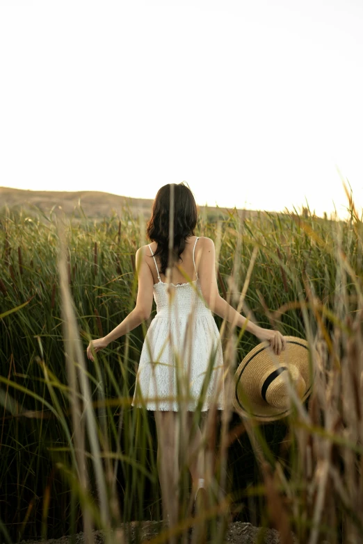 a girl in the field is holding a hat