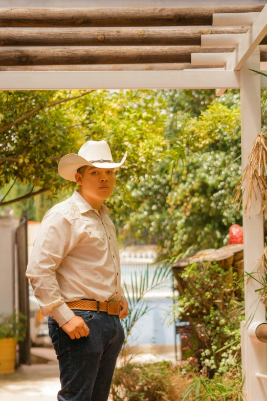 a man in white shirt and jeans standing by a wood trellis