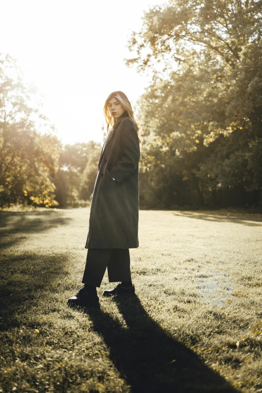 a woman standing in an open field with a tree and sunshine shining through the trees