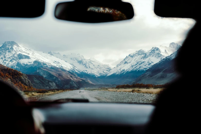 view of snowy mountains from the front window of a vehicle