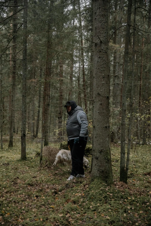 man in black hoodie standing near a tree with dog