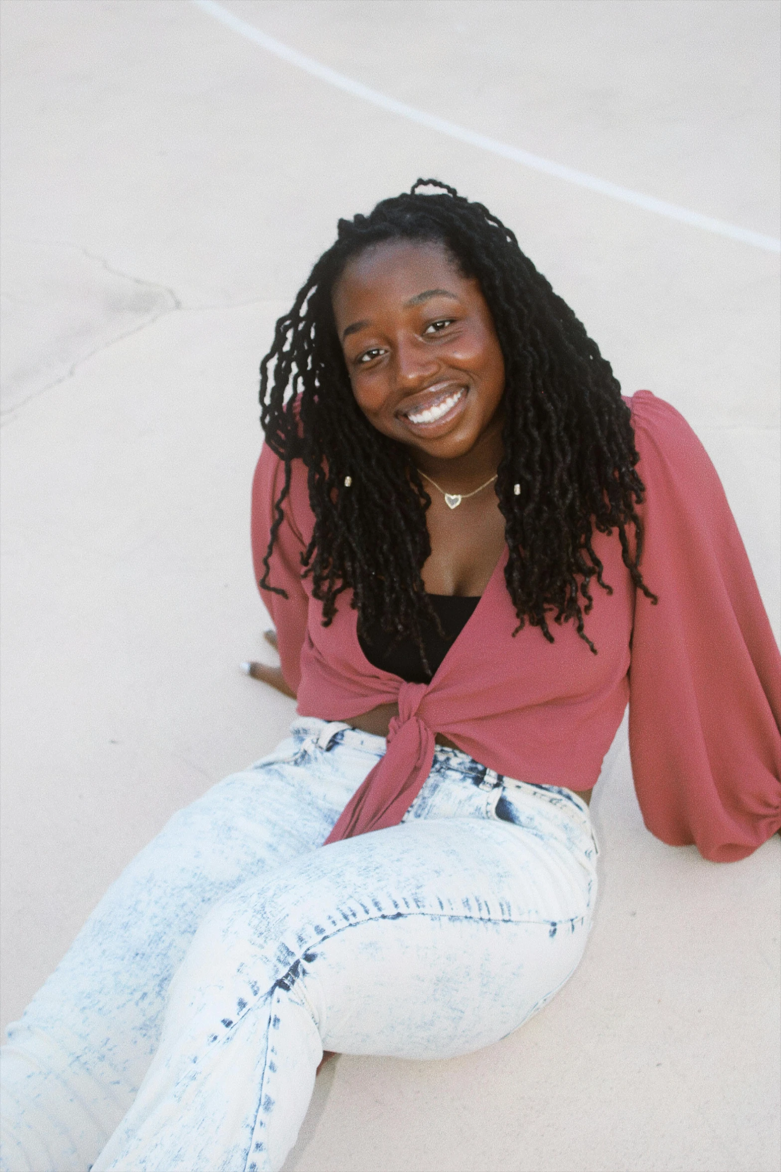 a smiling woman sitting on the ground with her legs crossed