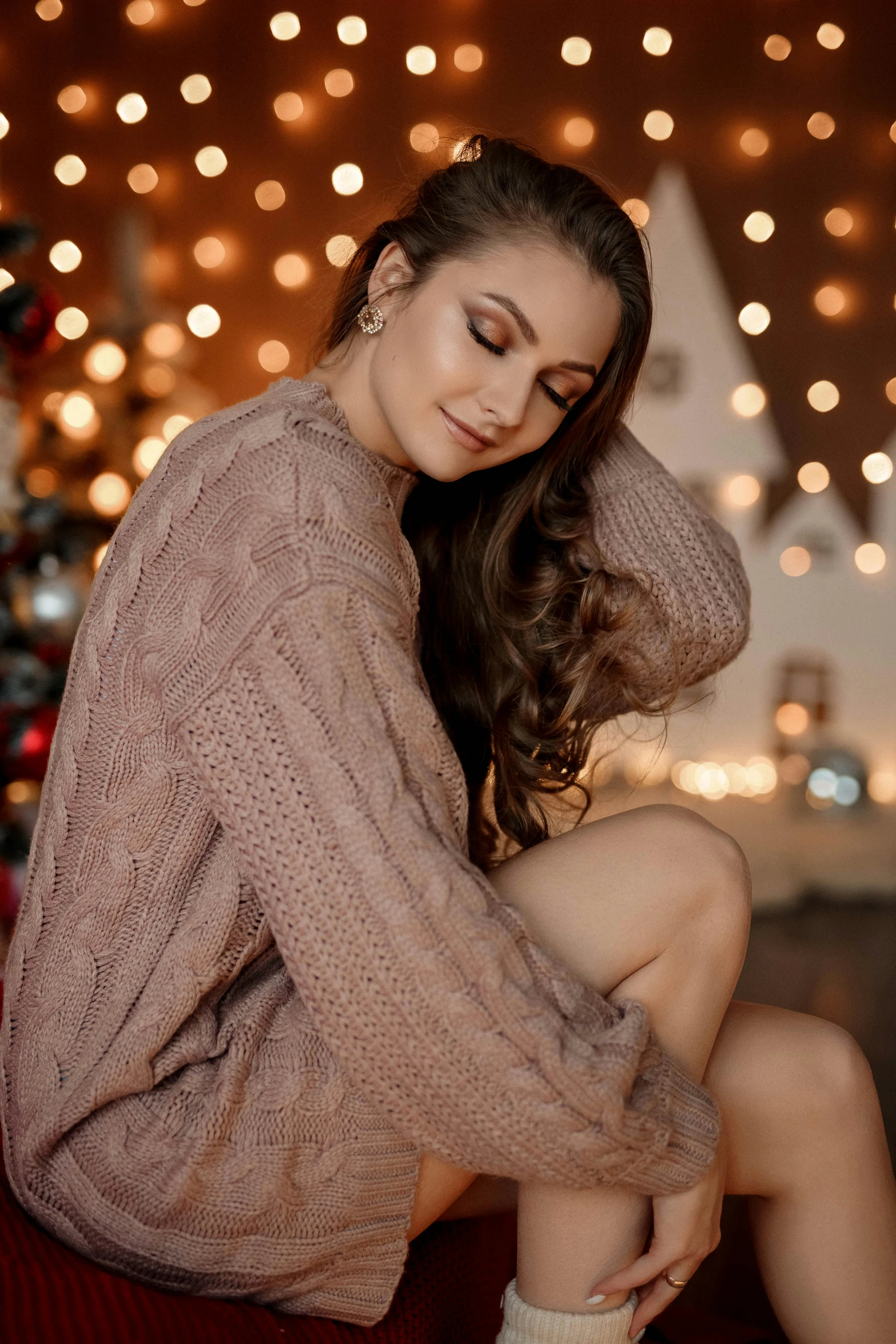 a woman in brown sweater sitting on couch next to christmas tree