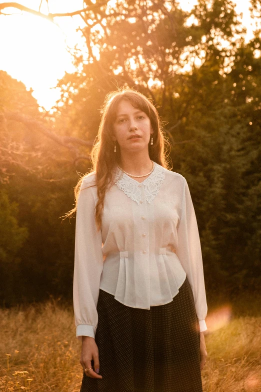 a woman standing in a field while wearing a white blouse