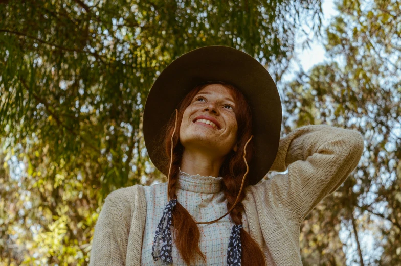 a person with long hair and a hat standing in front of trees