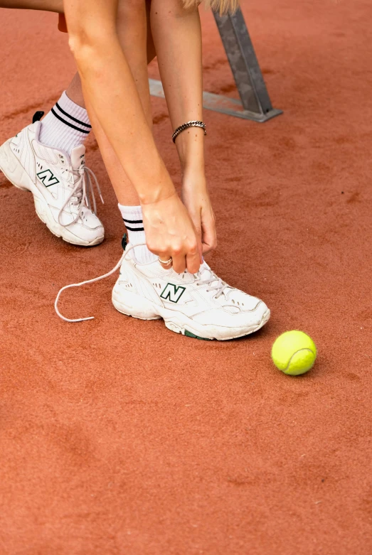 a person tying up a tennis ball with white tennis shoes