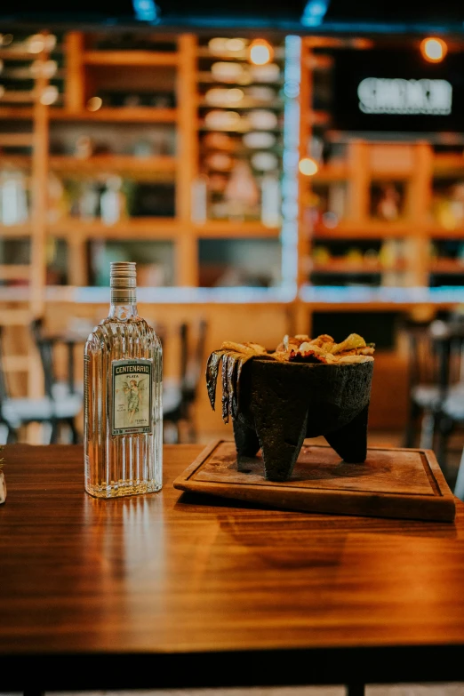 a bottle of gin and a glass bowl on a wooden table