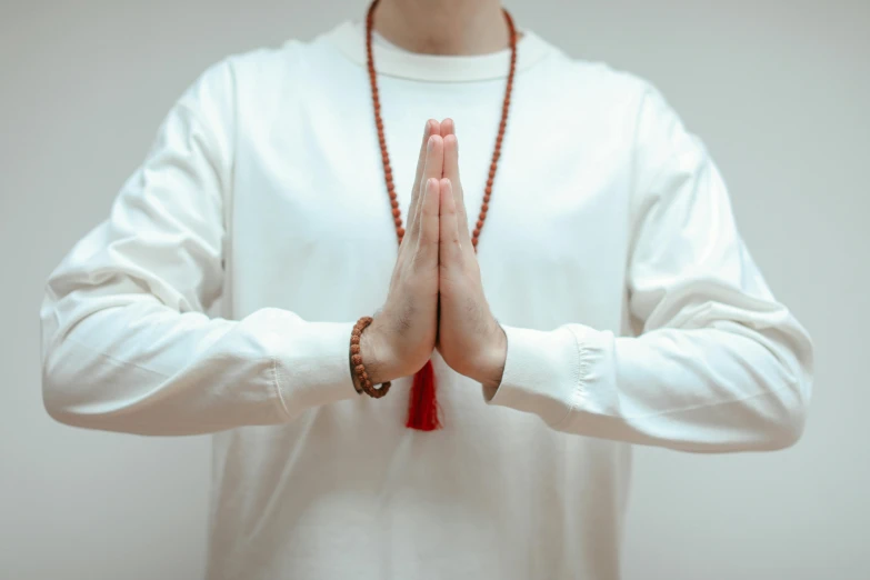 a person holding up their hands while wearing a long necklace